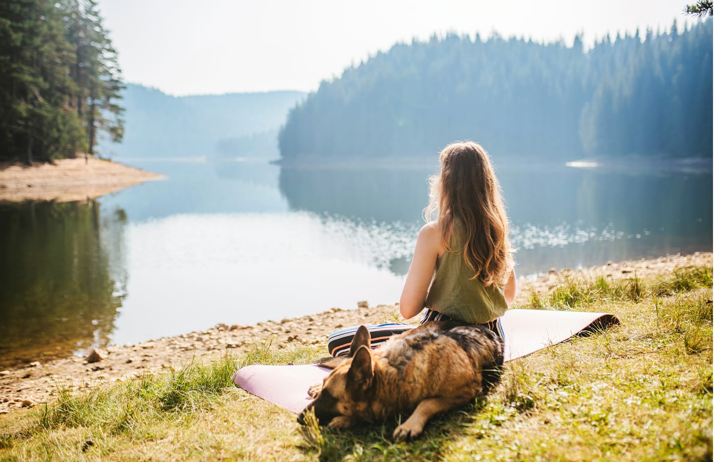 female sitting on a yoga mat by the lake with her dog next to her