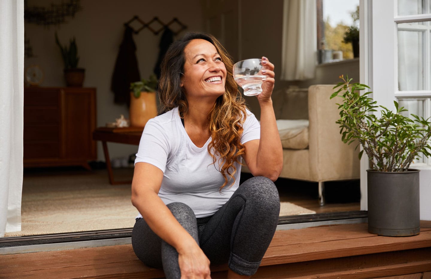 Female smiling sitting on a stair outside with a glass of water in hand