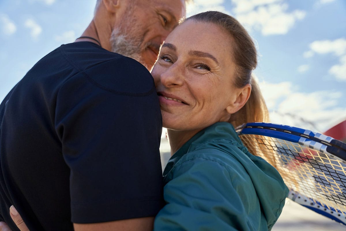 female and male smiling and hugging while holding tennis rackets